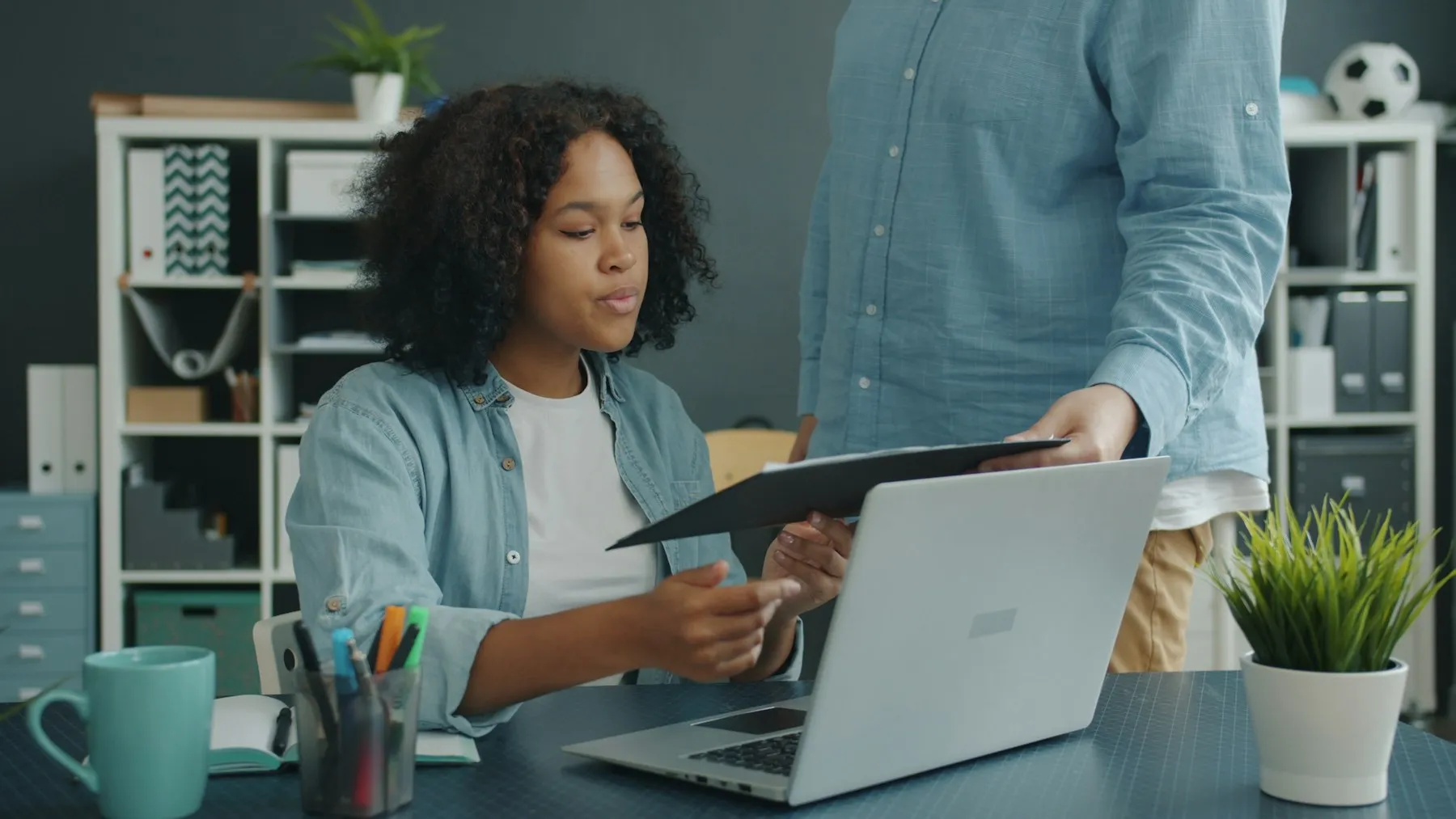 Un asesor le muestra un documento a una emprendedora que trabaja en su laptop