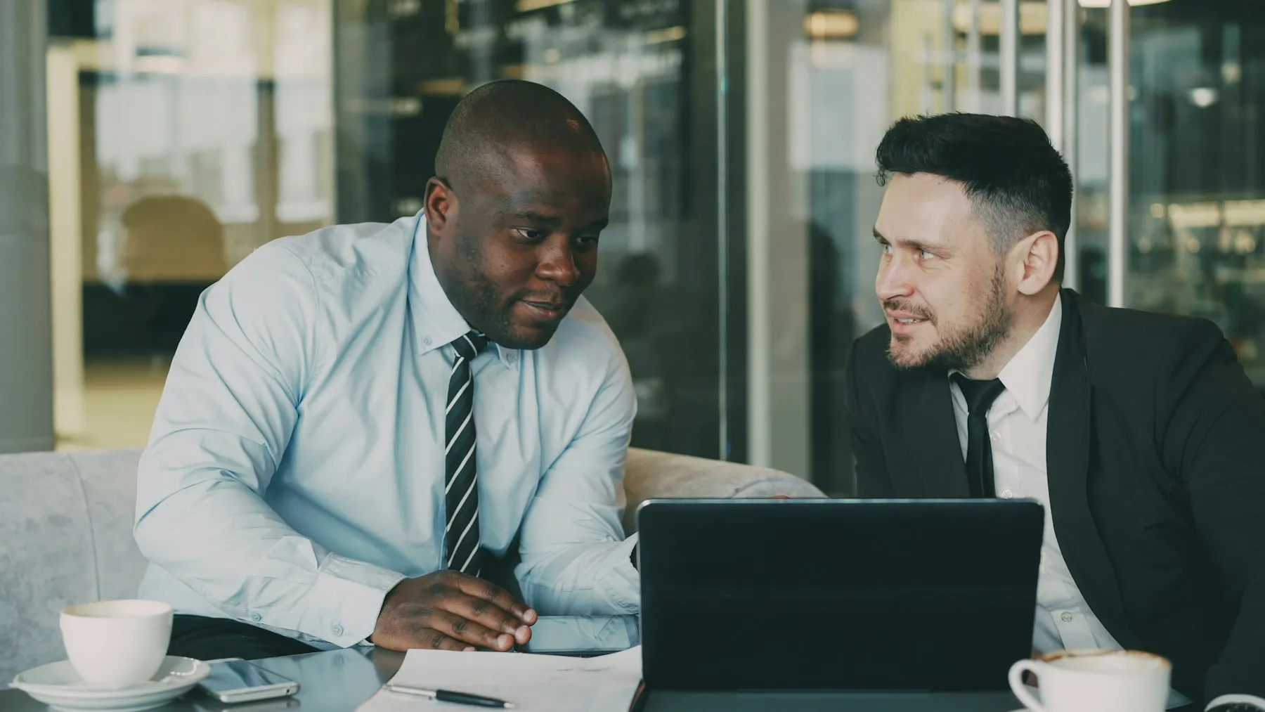 Dos personas conversando en una mesa con una laptop y café